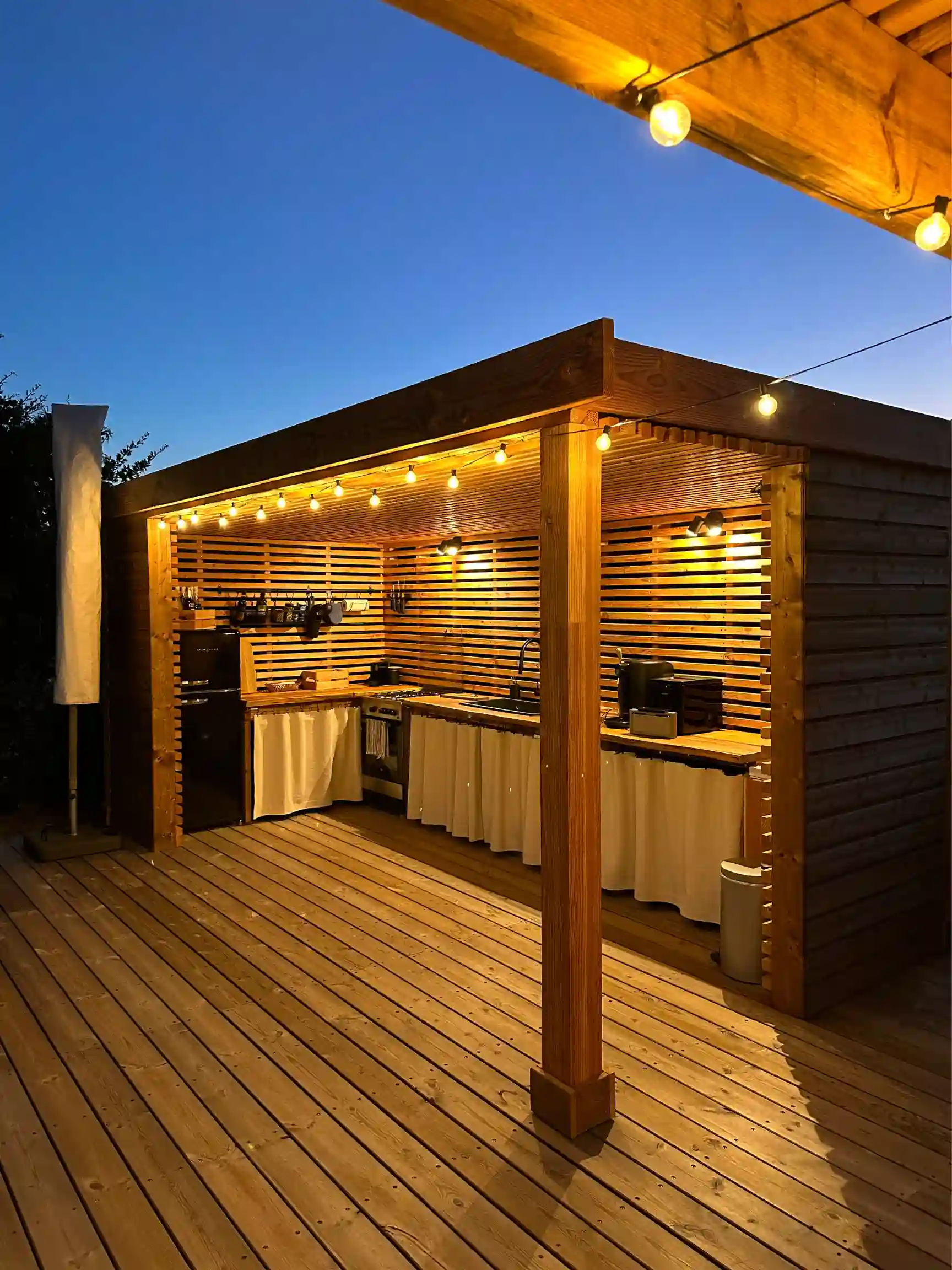 Conception d'une cuisine d'été extérieure (Pool House) en bois sur-mesure avec éclairage d'ambiance et terrasse en bois exotique à Hyères.