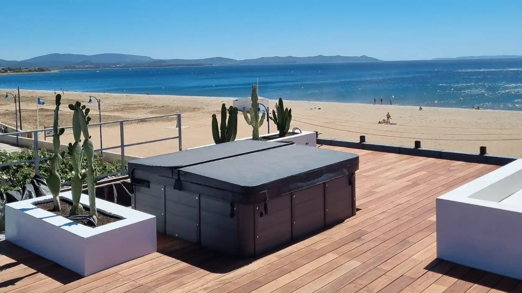 Toit-terrasse aménagé en bois exotique avec jacuzzi et jardinières de cactus, offrant une vue panoramique directe sur la plage et la mer à Hyères.