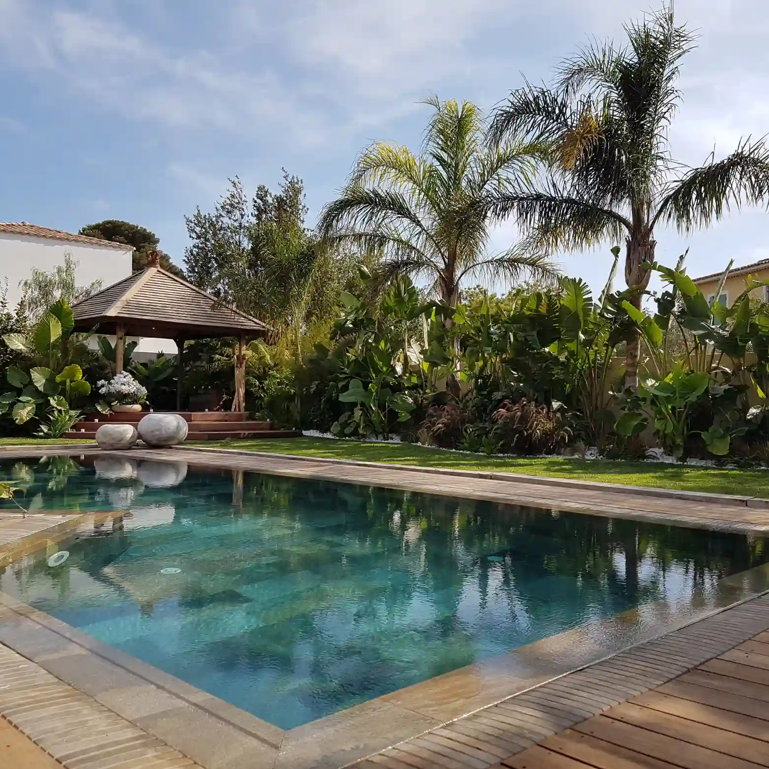 Piscine esprit Bali au revêtement en pierre naturelle (Green Sukabumi) avec plage en bois et margelles immergées, réalisée par un paysagiste à Hyères.