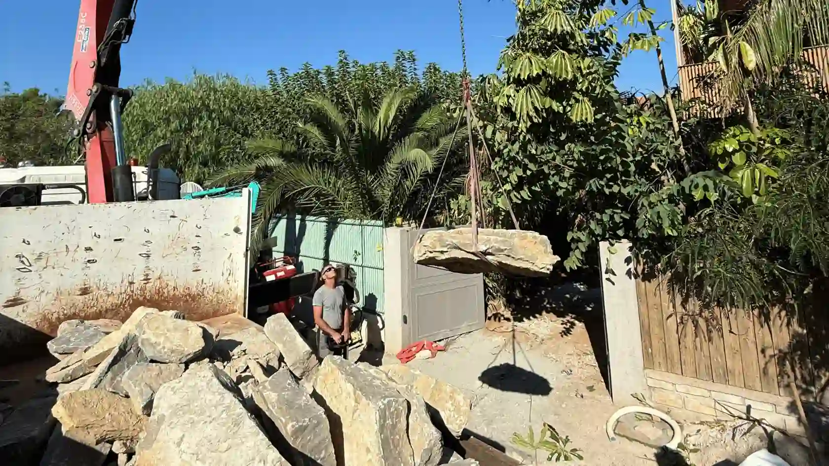 Réalisation d'une piscine lagon naturelle avec cascade en rocaille, entourée de plantations tropicales luxuriantes et d'une terrasse en bois au premier plan.