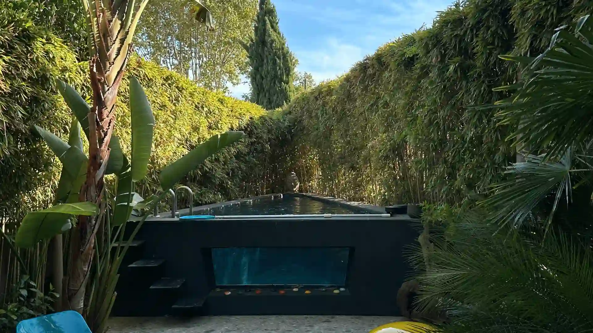 Vue d'un jardin avec une haie de bambous et de cyprès de très grande hauteur, taillée de manière rectiligne et impeccable, bordant un bassin moderne.