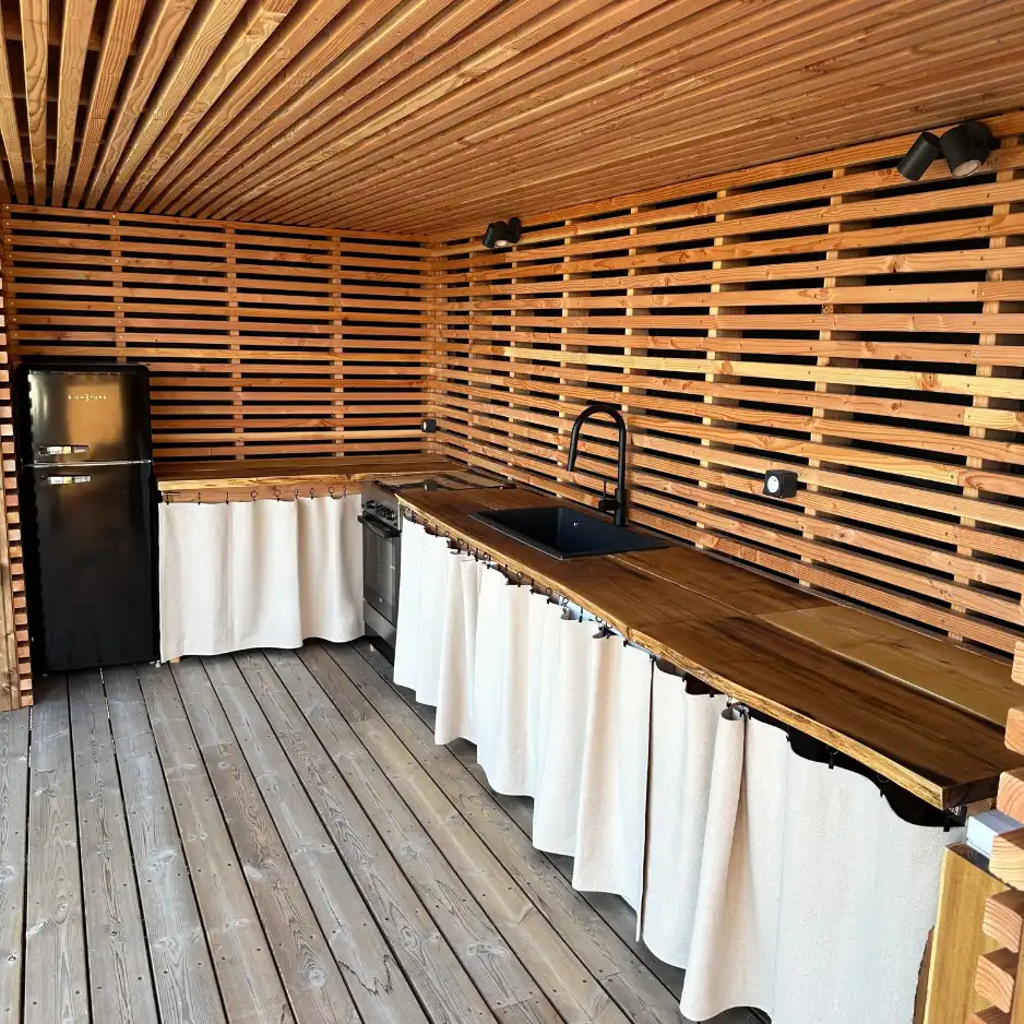 Aménagement d'une cuisine d'été moderne sous pergola en bois avec bardage ajouré et plan de travail en bois massif par L'Empreinte Verte dans le Var.