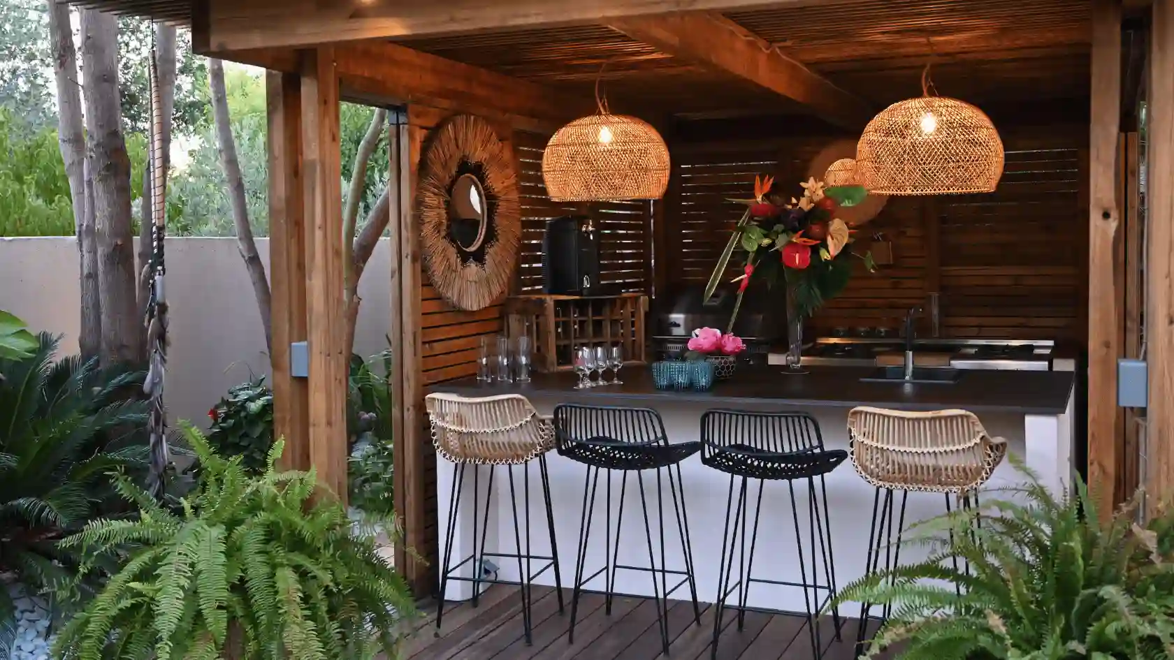Création d'une cuisine d'été luxueuse sous une pergola en bois : bar extérieur, luminaires en rotin et végétalisation exotique. Aménagement paysager haut de gamme dans le Var.