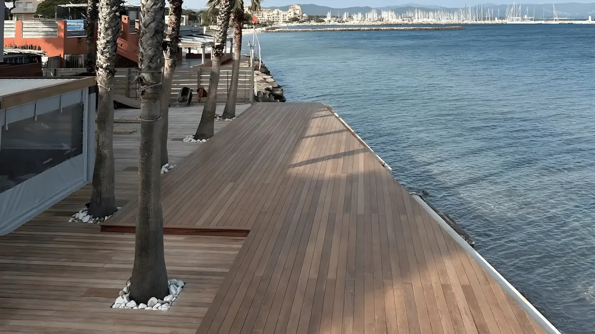 Réalisation d'une grande terrasse en bois exotique en bord de mer à l'Hôtel Bor (Hyères). Pose de lames de bois avec découpes précises autour des palmiers et vue panoramique sur la Méditerranée.