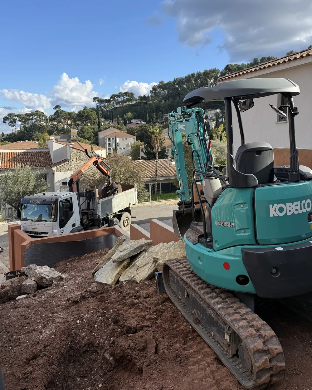 Chantier de terrassement avec mini-pelle et pierres de restanque, sur une propriété en pente dans le Var