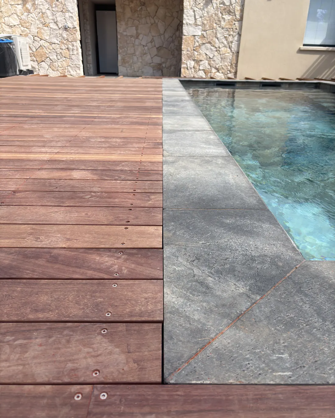 Terrasse en bois exotique en bordure de piscine, contraste avec la margelle en pierre, dans le Var